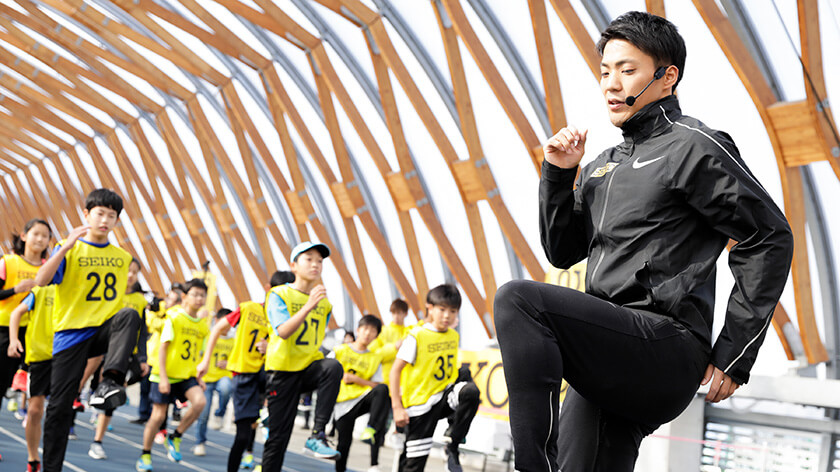 ウォーミングアップする子供たちと山縣亮太選手 写真