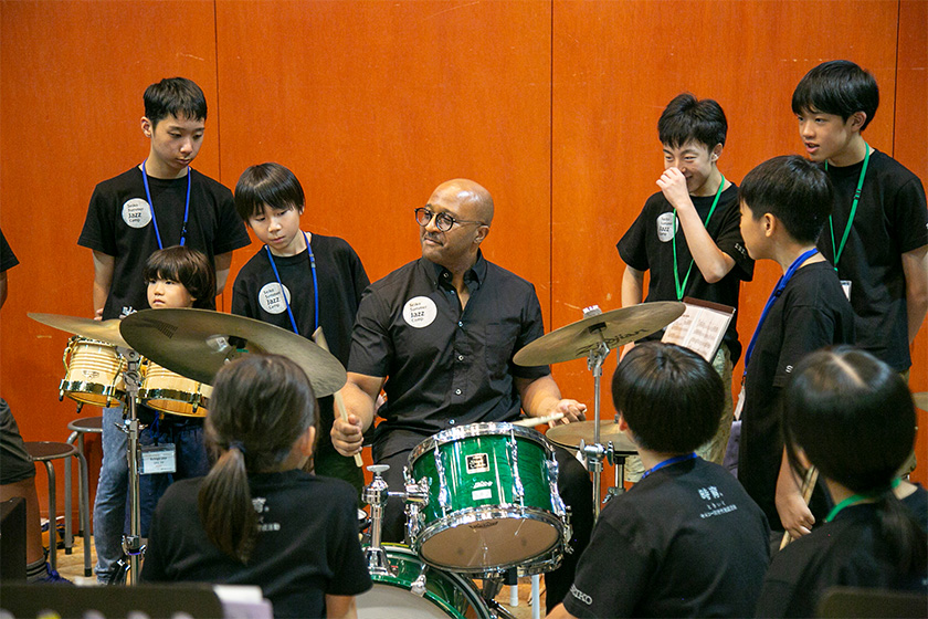 ドラムを演奏するクインシー・デイヴィスとドラムを囲む生徒たち