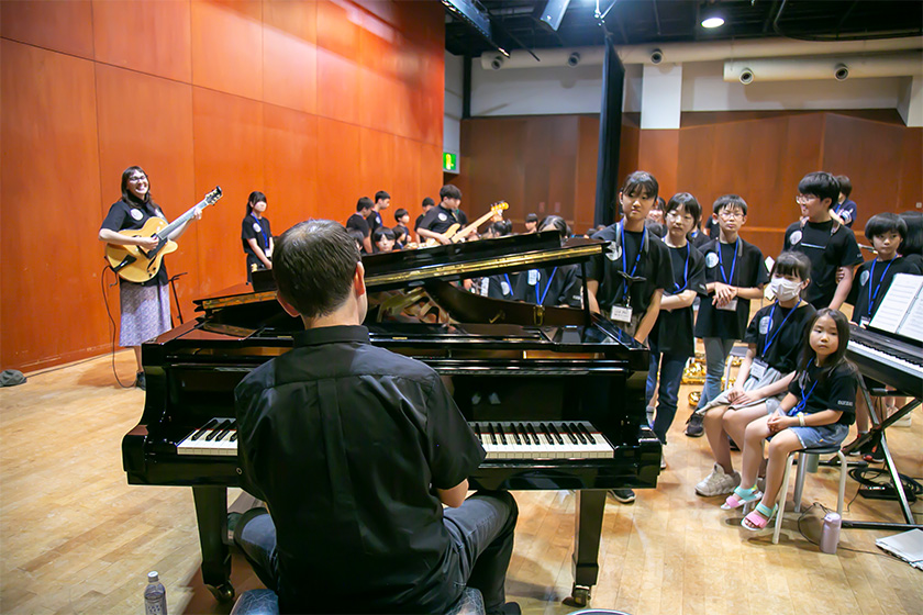 ピアノを演奏するダン・ニマーとピアノを囲む生徒たち